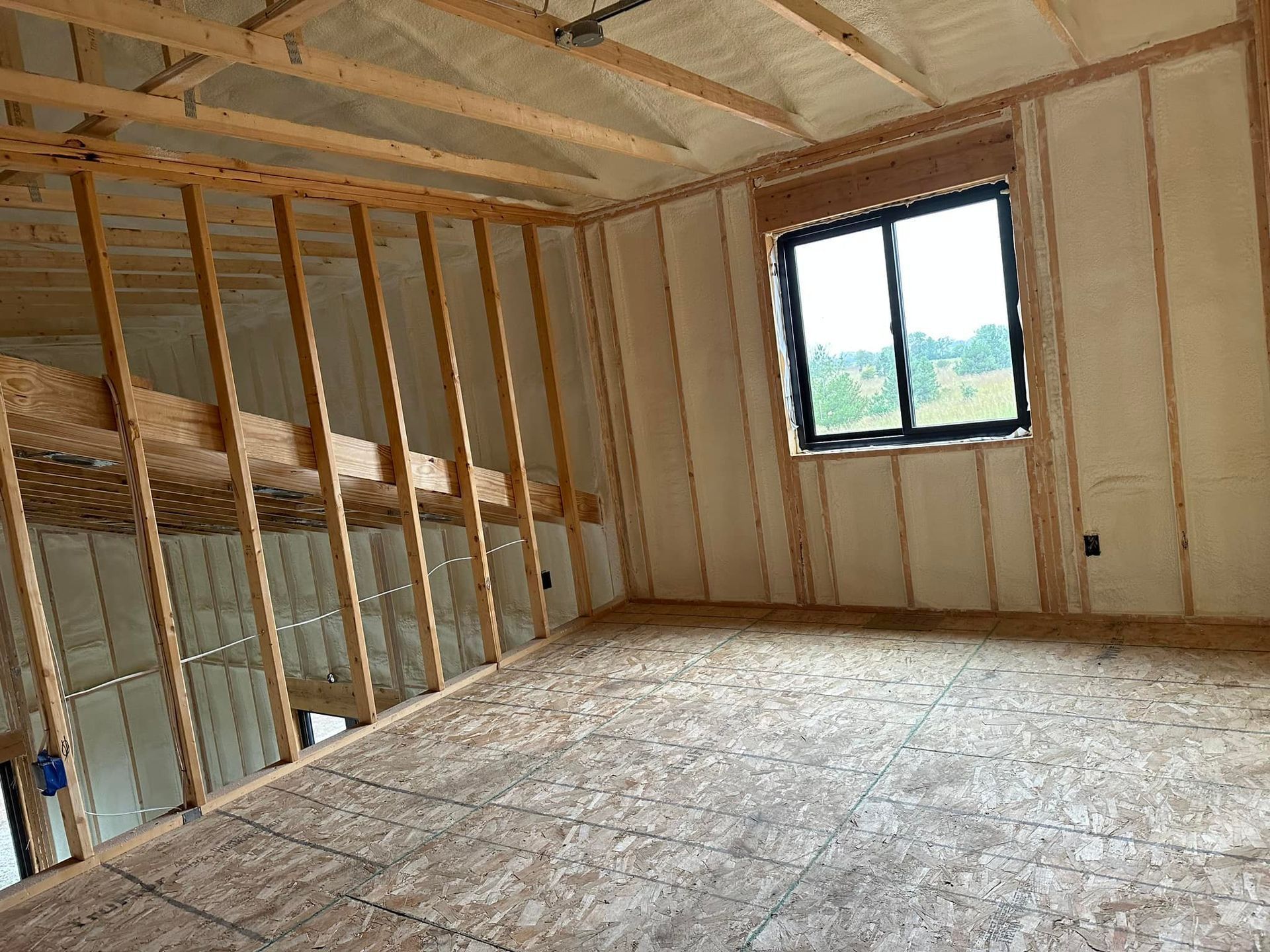 Framed interior room under construction with exposed studs, insulation, and a window.