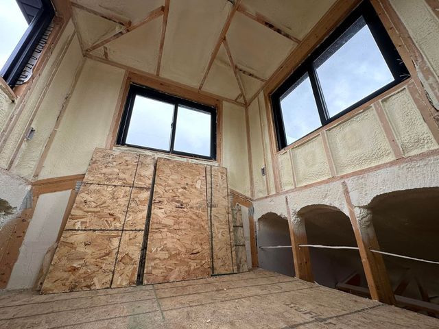 Partially finished room with exposed plywood walls, high windows, and built-in shelves under construction