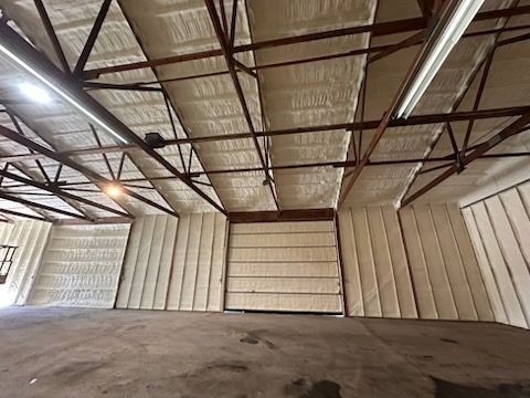 Empty warehouse interior with metal roof trusses and corrugated walls.