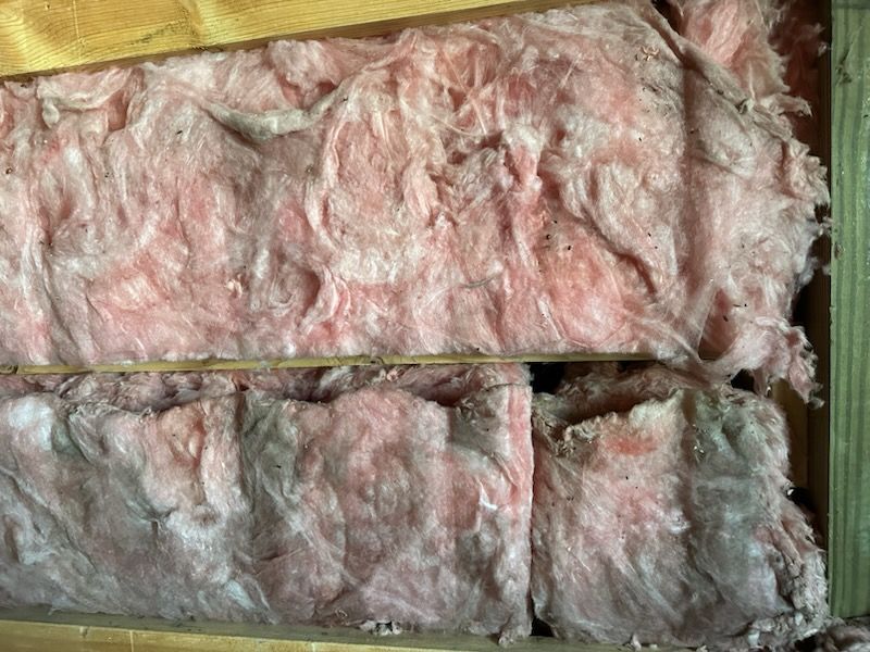 Pink and white fiberglass insulation stuffed between wooden framing boards