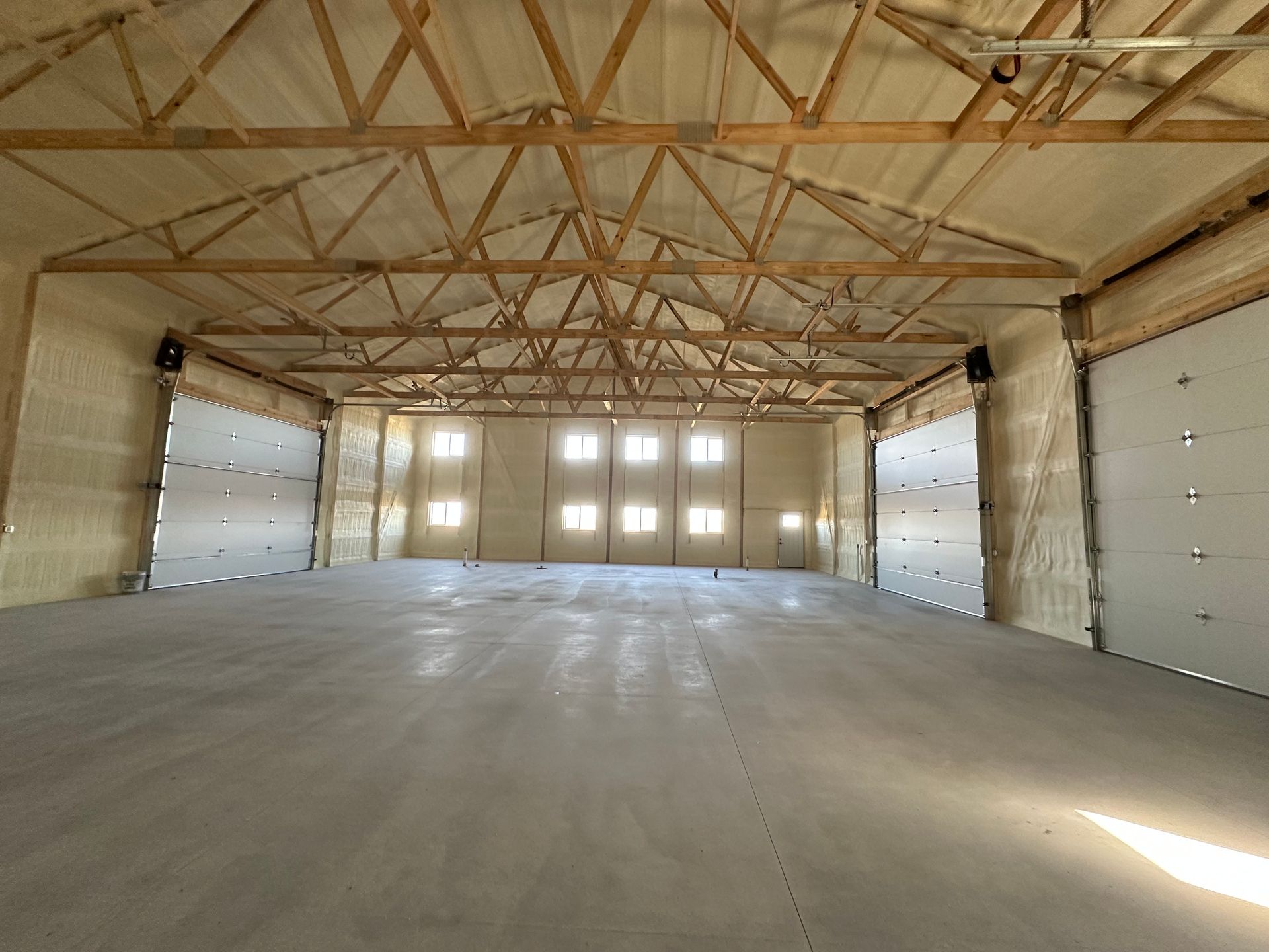 Empty industrial warehouse interior with concrete floor, exposed wooden trusses, and large garage doors