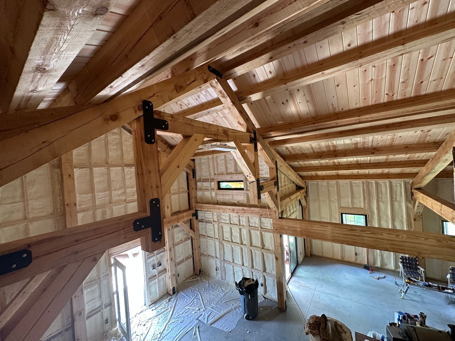 Wooden loft interior with exposed beams, slanted ceiling, and insulation panels under construction