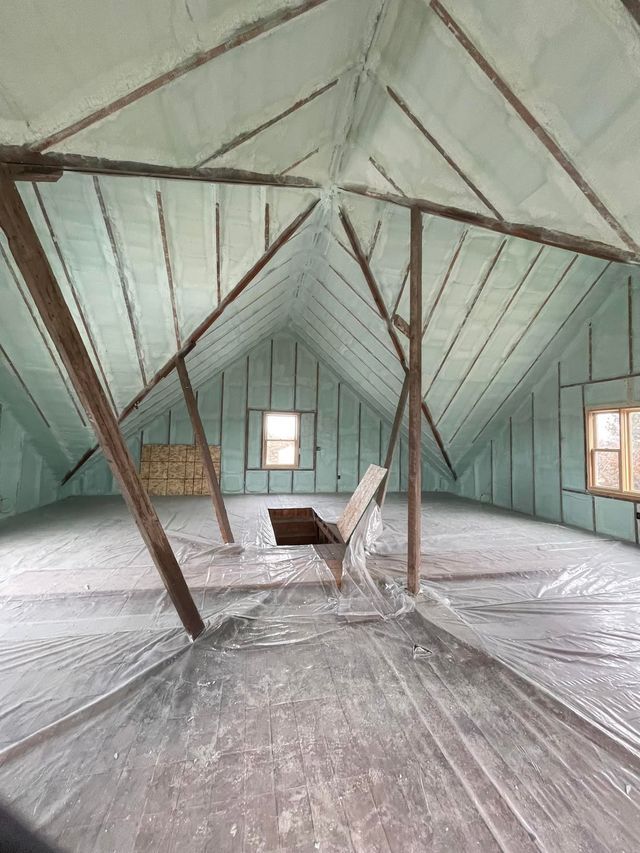 Empty attic with green painted walls, exposed rafters, small windows, and a central opening in the floor.